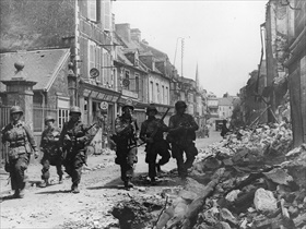 Battle of Carentan: 101st Airborne paratroopers walk Carentan street, mid-June 1944